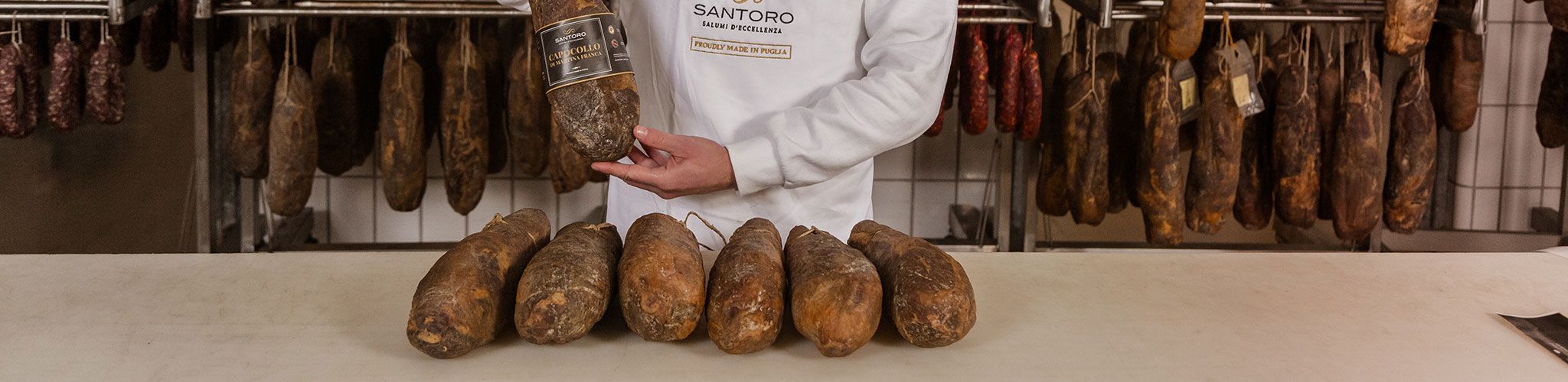 Hanged Santoro salami ready for the online sale and Capocollo in a worker's hands